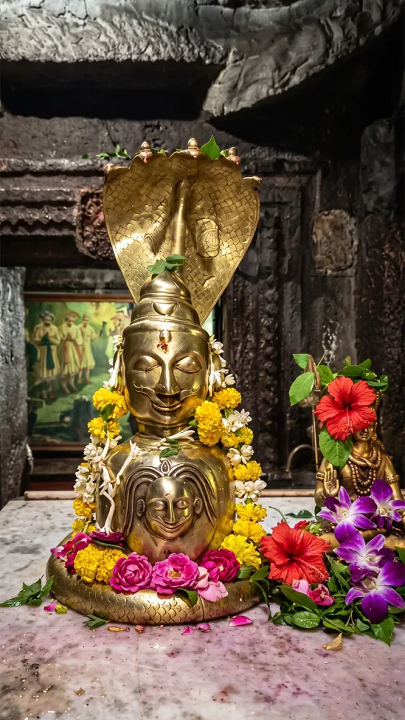 Brass Mukhalingam idol of Lord Shiva with Sheshnaag hood and flower offerings on a marble altar.