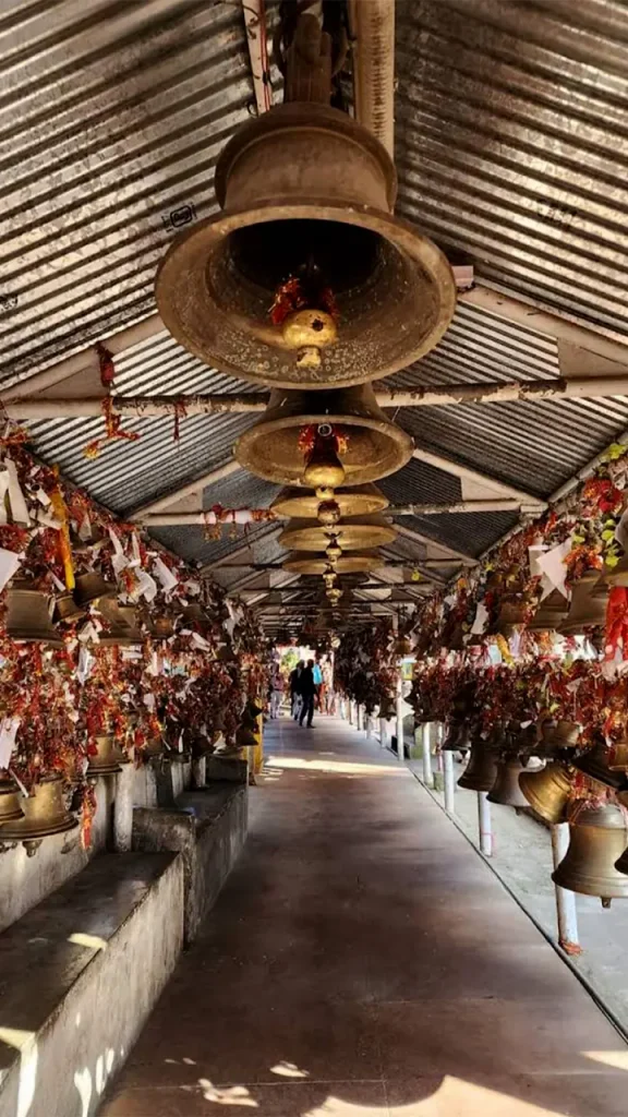 Souvenir and puja stalls selling brass bells outside Chitai temple entrance.