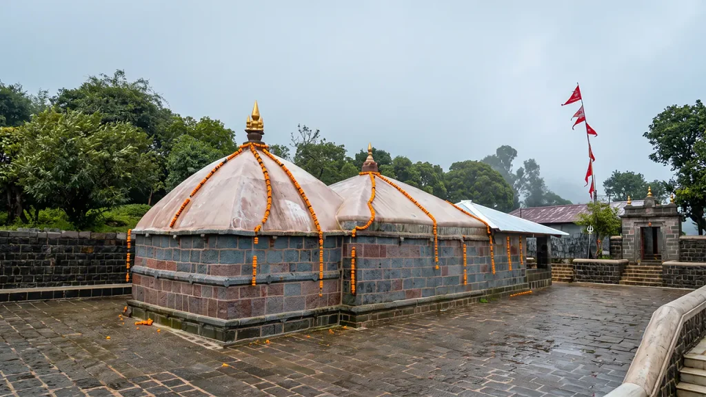 Ancient stone temple with domed roofs decorated with marigold garlands under an overcast sky.