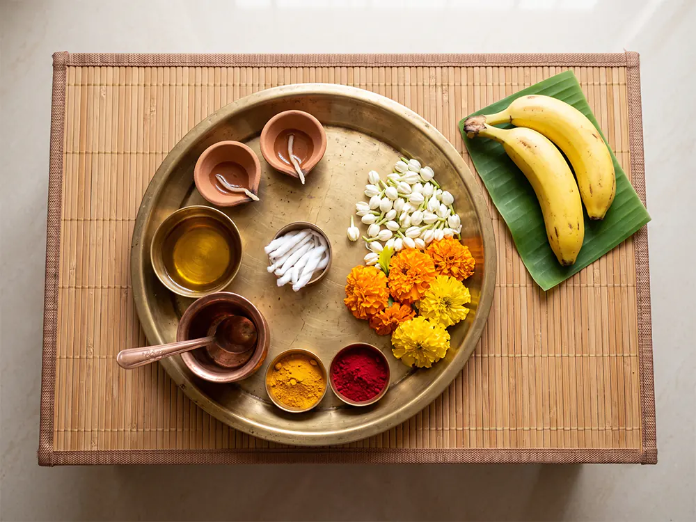 Neatly arranged Karthika Masam home pooja items including clay lamps, sesame oil, cotton wicks, flowers, fruit, and a small copper water cup